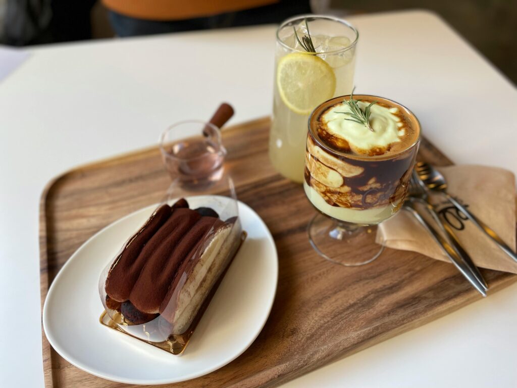 Close-up of a tiramisu and coffee on a wooden tray with lemon drink, creating a cozy food arrangement.