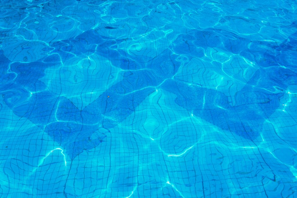Vibrant blue swimming pool water with sunlit reflections and ripples on a tiled surface.