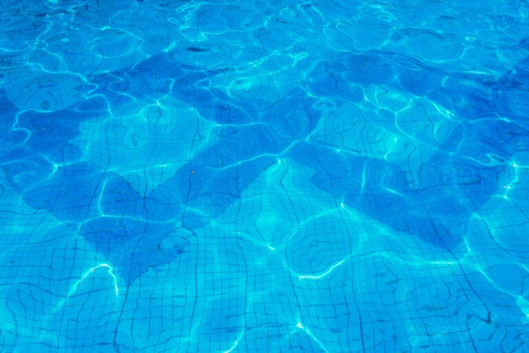 Vibrant blue swimming pool water with sunlit reflections and ripples on a tiled surface.